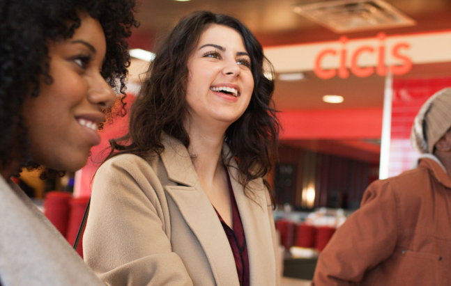A group of business people smile and chat as they sit together in a Cicis dining room. There is a lit up red "Cicis" sign behind them. 